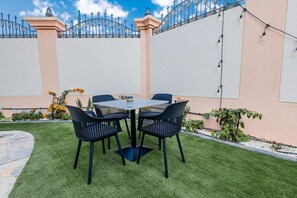 A patio with a round table and four chairs, surrounded by a well-maintained lawn and a decorative fence.
