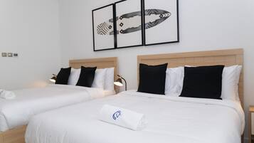 A hotel room with two beds, each with white bedding and black pillows. There is a framed artwork above the beds and a small table with a lamp beside the beds.