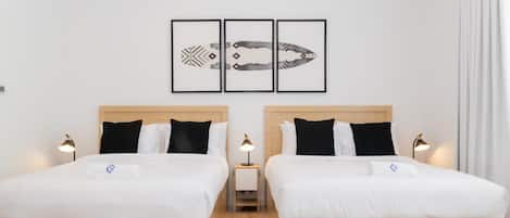 A hotel room with two beds, a wooden floor, and a wall with three framed artworks.