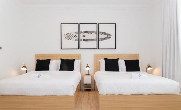 Habitación de hotel con dos camas, piso de madera y una pared con tres obras de arte enmarcadas.