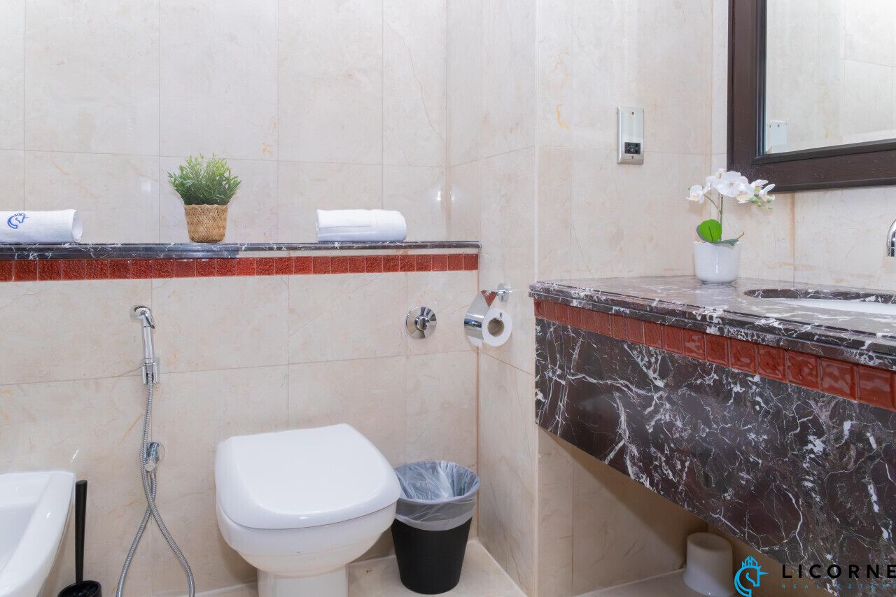 Une salle de bain avec un lavabo en marbre, des toilettes, une douche et une poubelle.