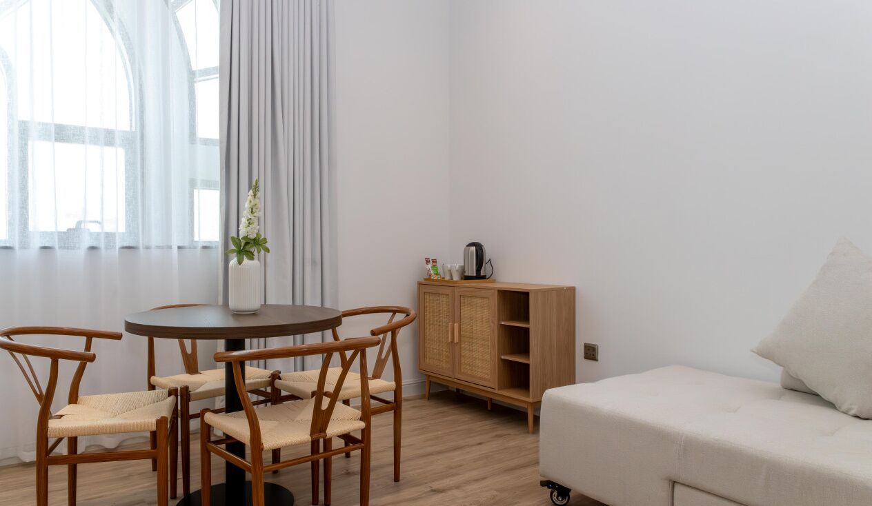 Een kamer met een ronde tafel, vier stoelen, een kast, een bank en een raam met gordijnen.