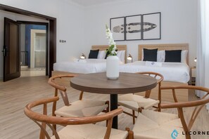 Habitación de hotel con dos camas, una mesa redonda de madera con sillas, un jarrón blanco con flores y cuadros en la pared.