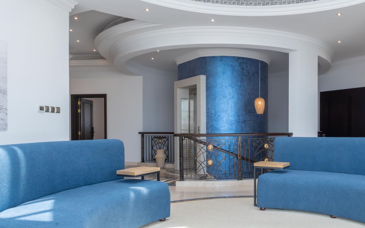 Eine Lobby mit blauer Akzentwand, einer Treppe mit aufwendiger Geländer und zwei blauen Sofas.