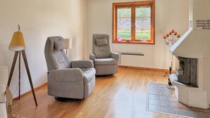 Una sala de estar con dos sofás grises, una lámpara de pie, una chimenea y un ventanal con vistas a zonas verdes.