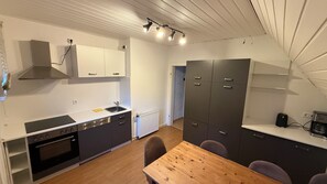 Cocina compacta con estufa, lavaplatos y armarios, una mesa de comedor con sillas y un refrigerador pequeño.