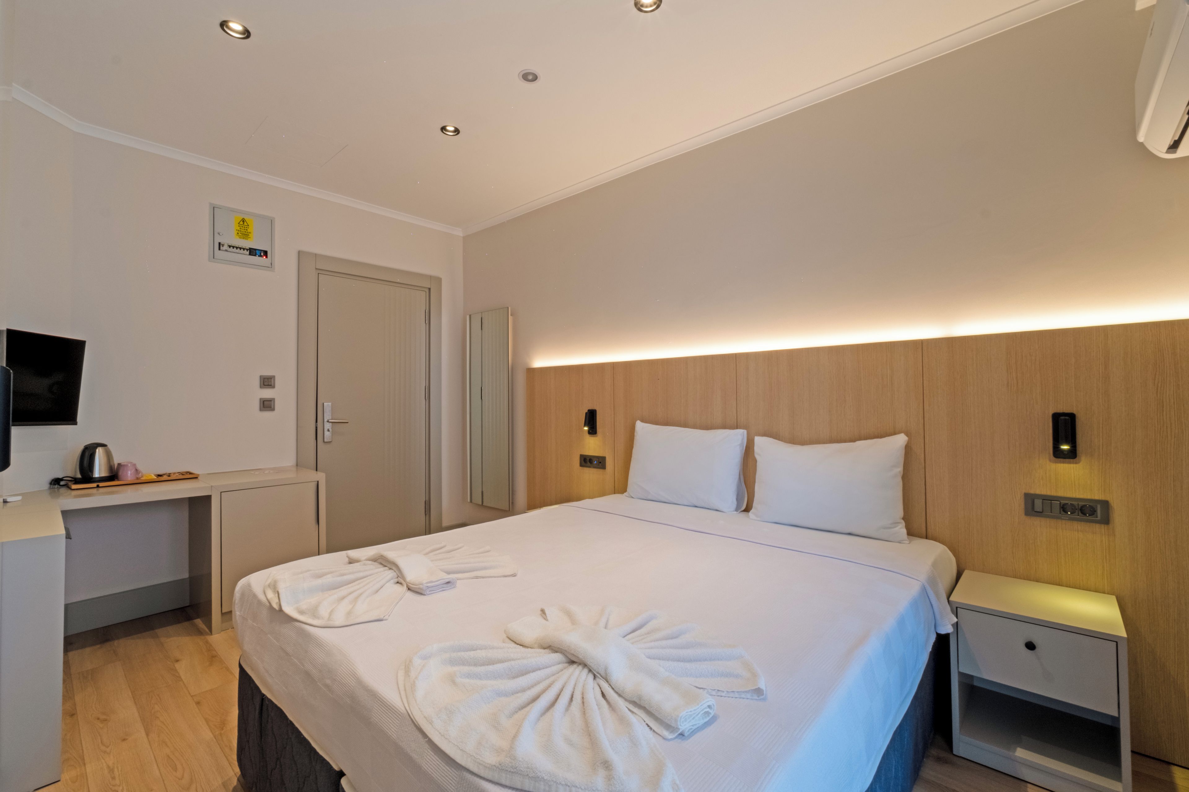 Una habitación de hotel con una cama, mesitas de noche, un televisor y un panel de control en la pared.