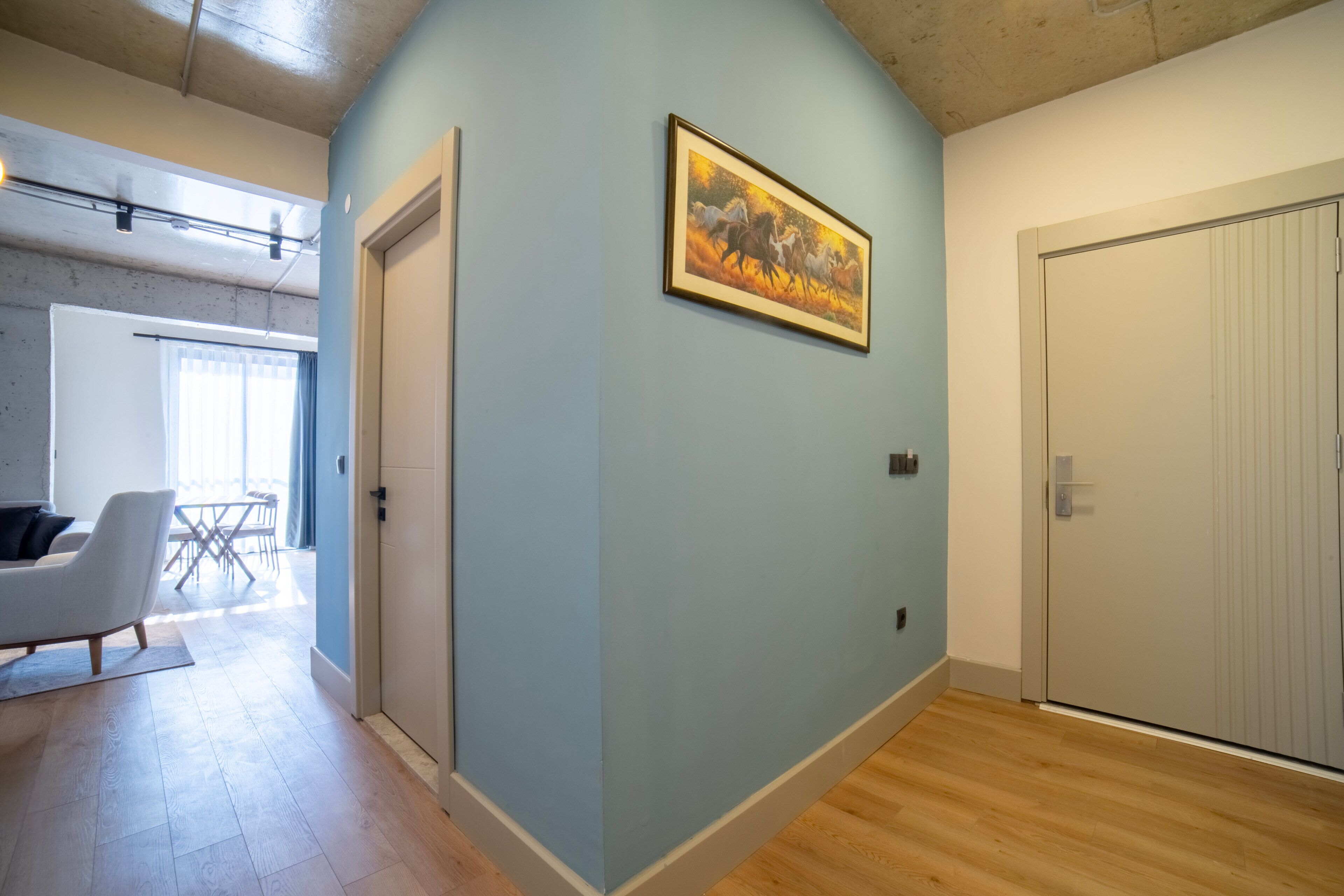 Una habitación con pared azul claro, un cuadro enmarcado, una puerta blanca y suelo de madera.