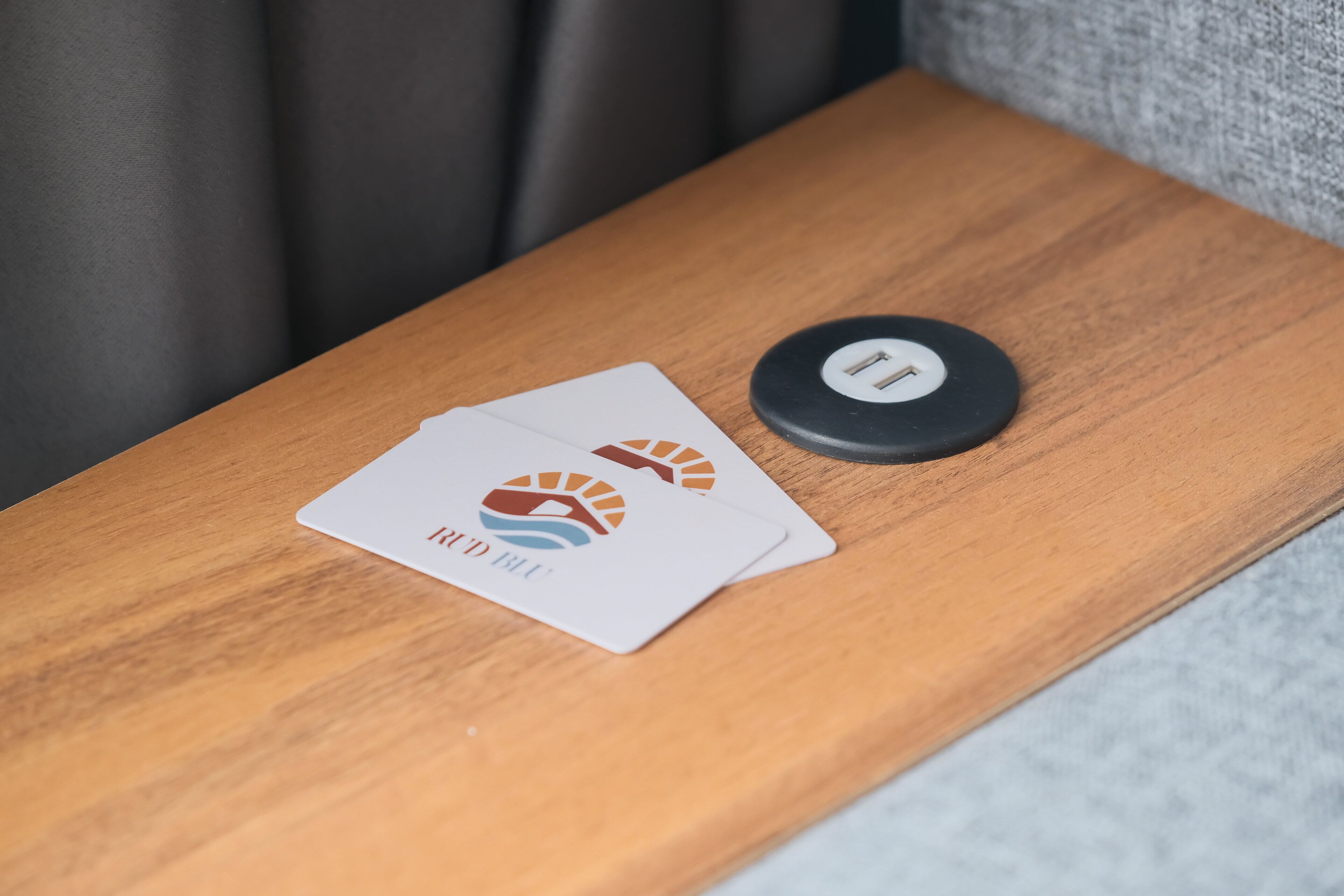 Een houten bijzettafeltje met twee visitekaartjes en een zwart voorwerp erop.