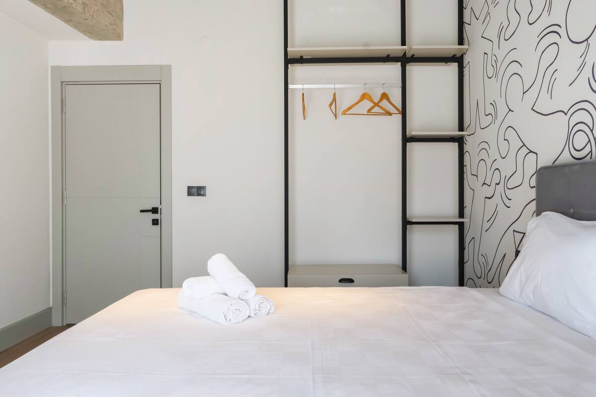A hotel room with a bed, a wardrobe with hanging space, and a door.