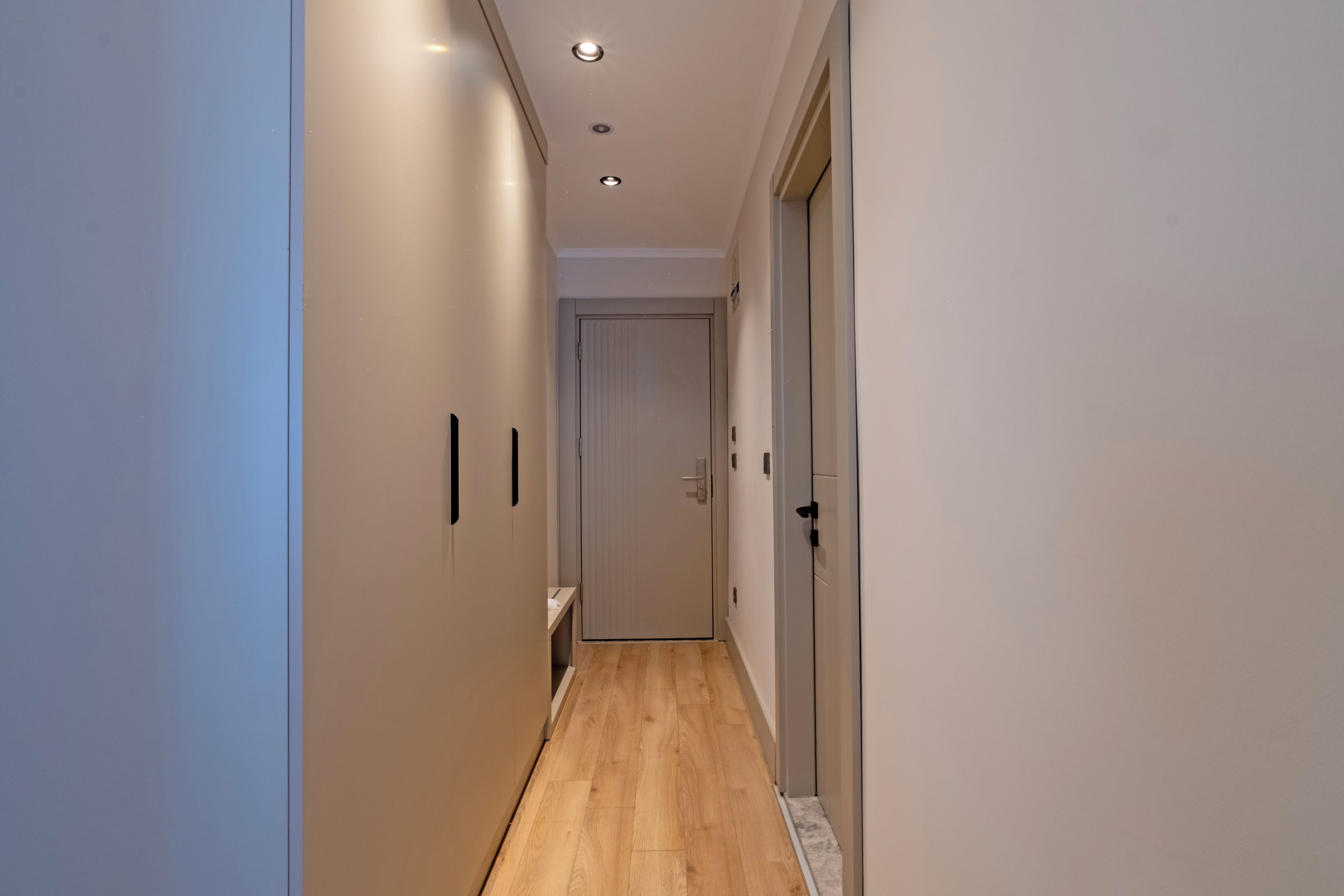 A narrow hallway with wooden flooring, white walls, and a door at the end.