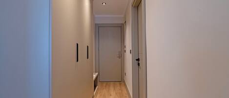 A narrow hallway with wooden flooring, white walls, and a door at the end.