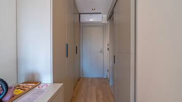Un pasillo estrecho con suelo de madera, una puerta blanca al final y una pequeña mesa con una bandeja de objetos a la izquierda.