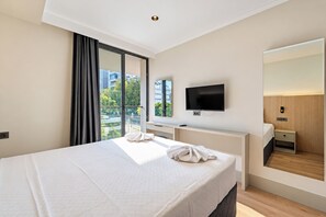 A modern hotel room with a large bed, a flat-screen TV, a large mirror, and a view of the city through the window. - Rudblu Suites (Konyaalti)