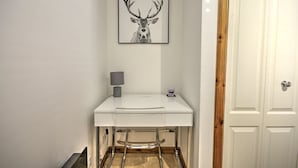 A white desk with a lamp and a framed deer head picture above it.