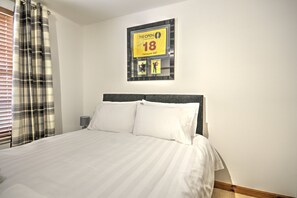 Quarto de hotel com uma cama, um quadro na parede e uma janela com persianas.