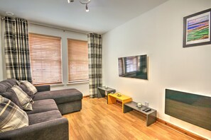 Uma sala de estar moderna com um sofá cinza, piso de madeira, uma mesinha e uma TV fixada na parede.
