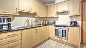 A modern kitchen with light wood cabinets, stainless steel appliances, and a tiled backsplash.