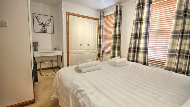 A bedroom with a large bed, a bedside table, a mirror, a door, and plaid curtains.