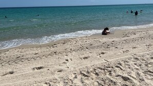 En sandstrand med fotspår och en person som sitter på sanden.