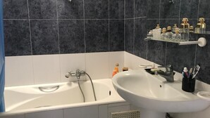 Ett badrum med badkar, handfat och spegel. På en hylla ovanför handfatet finns toalettartiklar.