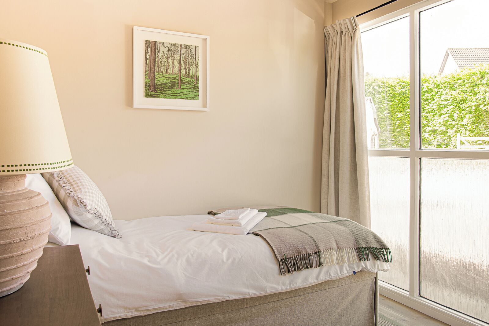 Ein ordentlich bezogenes Bett mit Decke, Kissen und einem gerahmten Bild an der Wand.