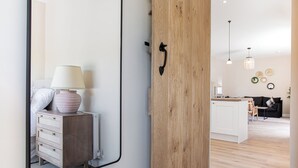 Um interior moderno com porta de madeira, um espelho refletindo um quarto com cômoda, luminária e cama.