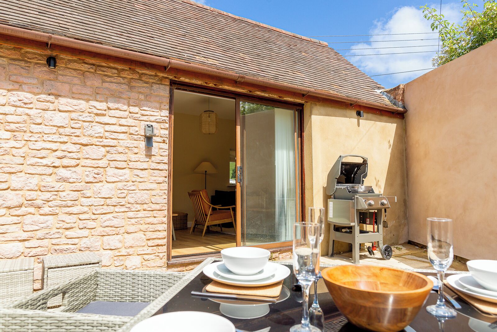 A stone building with a patio area, a grill, and a dining table set for a meal.