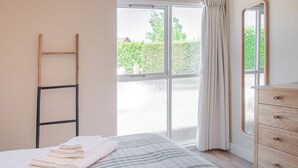 Quarto com cama, cómoda de madeira, janela com cortinas e vista para o verde lá fora.