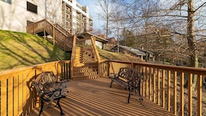 Eine Holzterrasse mit zwei Bänken, einer Treppe zu einem Gebäude sowie Blick auf Bäume und ein Gebäude im Hintergrund.