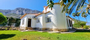 Set amidst lush greenery and mountains, this serene property features a symmetrical facade with a central entrance and two windows.