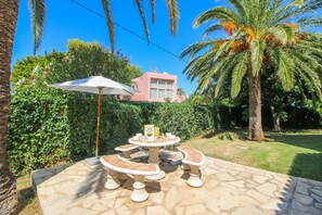 Relax in a serene patio setting surrounded by lush greenery and palm trees, complete with a stone table and benches.
