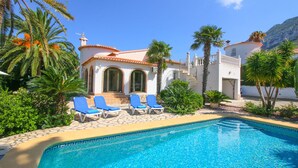 A poolside area with a clear blue pool, white building with arched windows, and palm trees. - All inclusive villa in Denia with pool 4p (Denia)