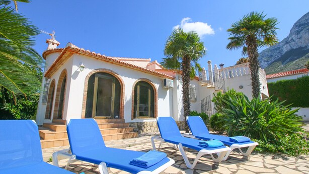 A building with a tiled roof and arched windows, surrounded by palm trees and lounge chairs. - All inclusive villa in Denia with pool 4p (Denia)
