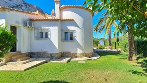 A white building with a stone base, two windows with metal bars, and a small staircase leading to the entrance. - All inclusive villa in Denia with pool 4p (Denia)