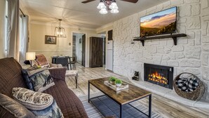 A living room with a stone wall, fireplace, and a ceiling fan. - Modern Style 2 Bed Condo Pool in Gatlinburg (Gatlinburg)