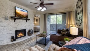 A living room with a stone fireplace, a ceiling fan, a large clock, and a view through a sliding glass door. - Modern Style 2 Bed Condo Pool in Gatlinburg (Gatlinburg)
