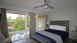 A bedroom with a large window, a bed, a bench, a ceiling fan, and a nightstand. - Amazing Lakefront Getaway (Hot Springs)