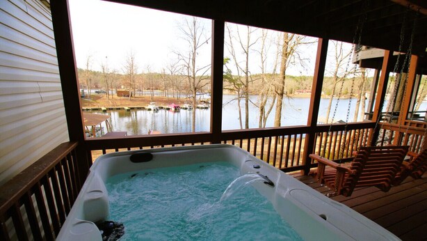 A hot tub on a wooden deck with a view of a lake and docked boats. - Amazing Lakefront Getaway (Hot Springs)
