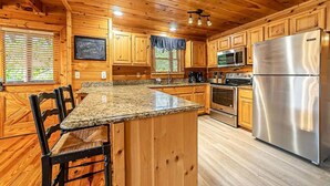 Una cocina de estilo cabaña de madera con encimeras de granito, un refrigerador de acero inoxidable y armarios de madera.