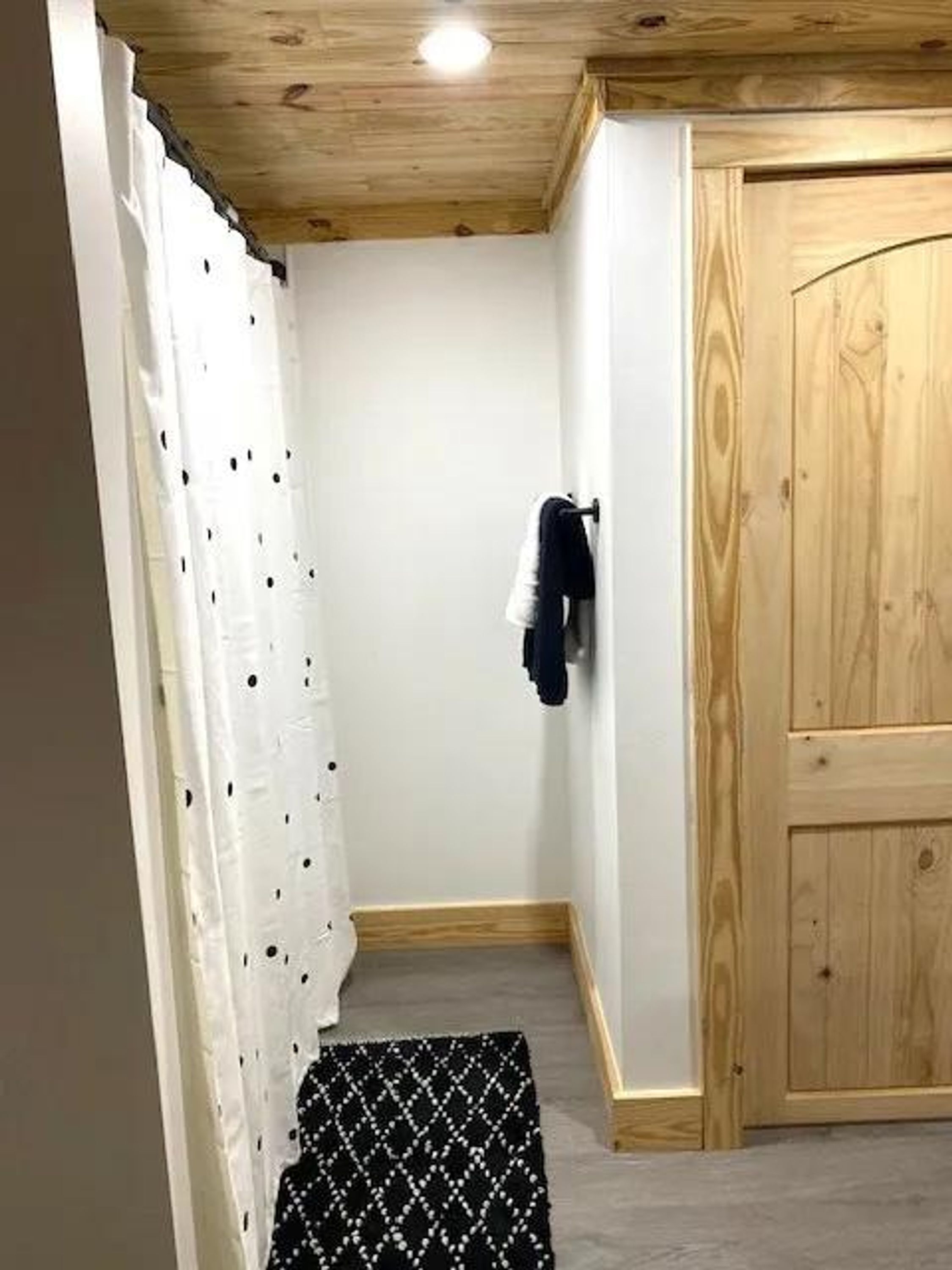 Una habitación con techo de madera, una puerta blanca y un tapete estampado en el suelo.