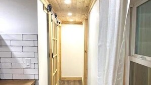 Un couloir étroit avec un plancher en bois, un mur en briques blanches et un plafond en bois.