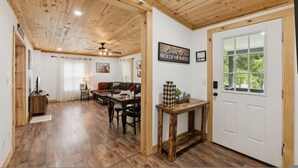 Une pièce spacieuse avec un plafond en bois, un coin repas comprenant une table et des chaises, un canapé et une porte avec une fenêtre.