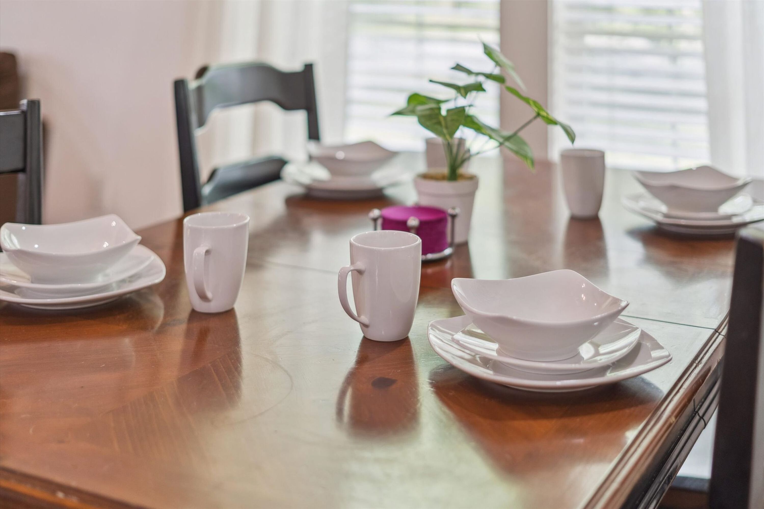 A dining table set with white plates, bowls, and a pink mug.