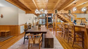 A spacious wooden interior with a long dining table, chairs, a staircase, and a kitchen area. - High-end Luxury Cabin Sauna Hot Tub Gameroom (Sevierville)