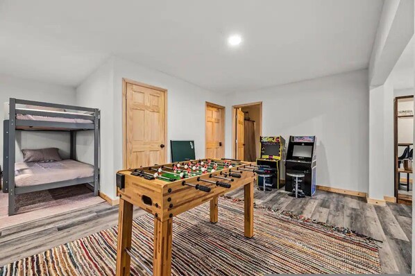 A room with a bunk bed, a foosball table, and a gaming console.