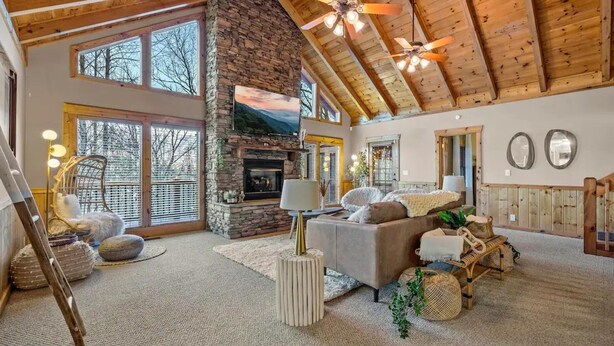 A spacious living room with a stone fireplace, large windows, and a high wooden ceiling. - High-end Luxury Cabin Sauna Hot Tub Gameroom (Sevierville)