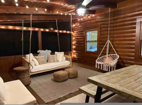 Interior acogedor de una cabaña de troncos, con una mecedora, una mesa de madera y un sofá con cojines.