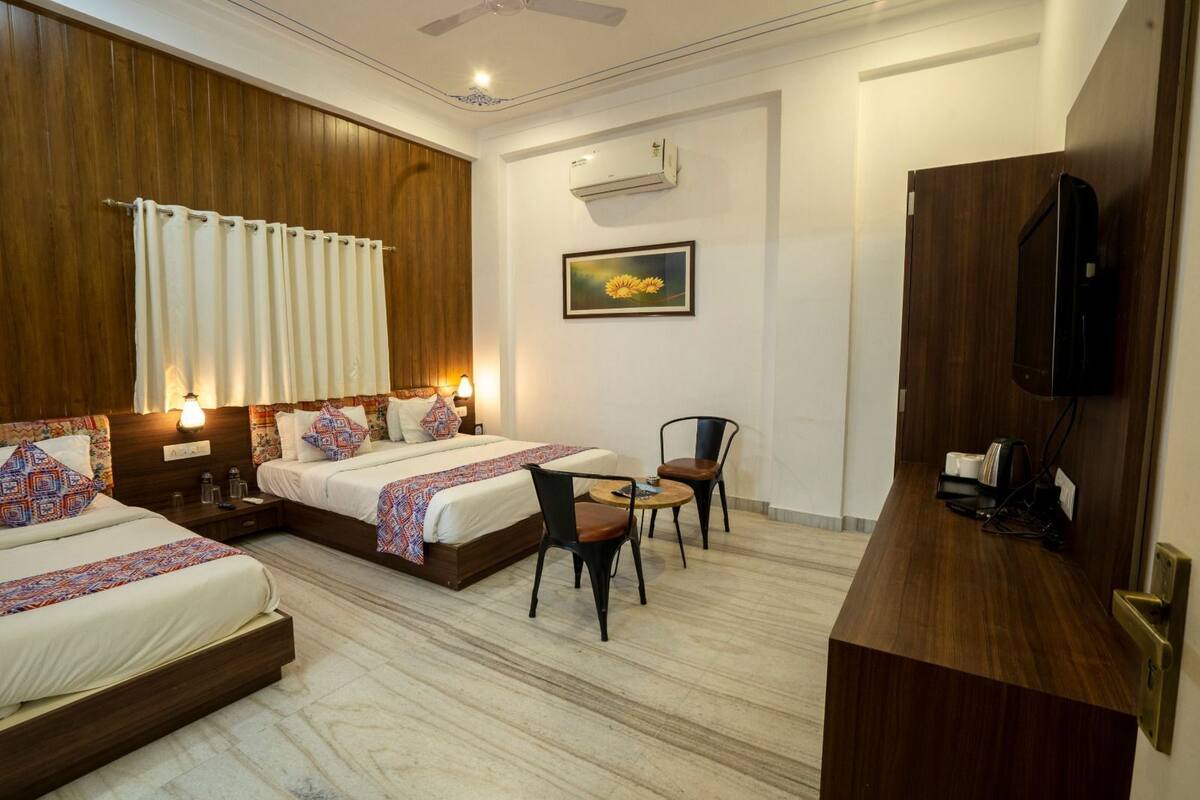Une chambre d’hôtel avec deux lits, une petite table avec des chaises, un téléviseur et un appareil de climatisation.