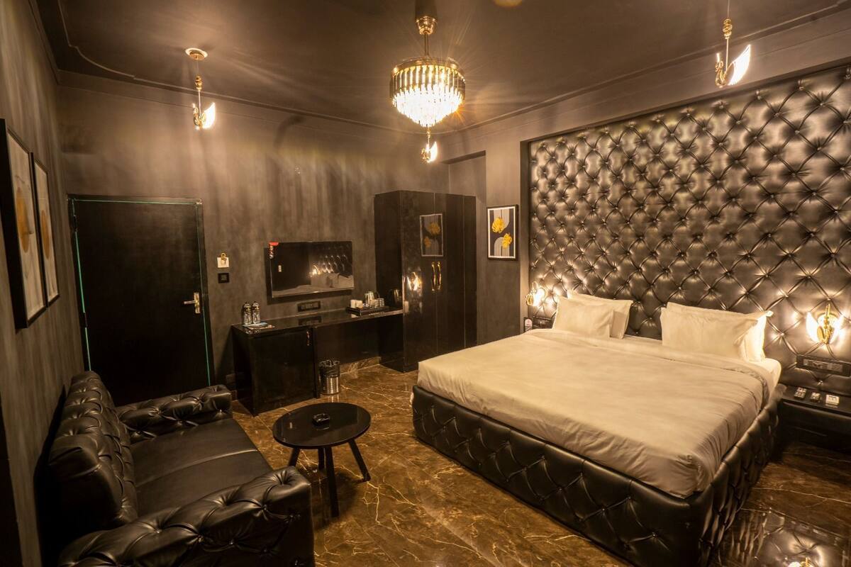 Une chambre luxueuse dotée d’une tête de lit capitonnée, d’un grand lit, d’un coin salon avec un canapé et une table basse, et d’un téléviseur fixé au mur.